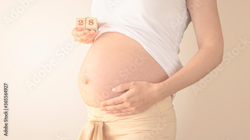 Pregnant young woman with pregnancy week number next to her belly. Photos of belly growth at 28 weeks pregnancy. Healthy pregnancy diet and fetal development. photo