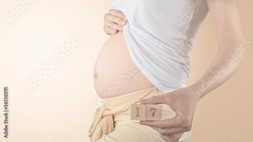 Pregnant young woman with pregnancy week number next to her belly. Photos of belly growth at 17 weeks pregnancy. Healthy pregnancy diet and fetal development.