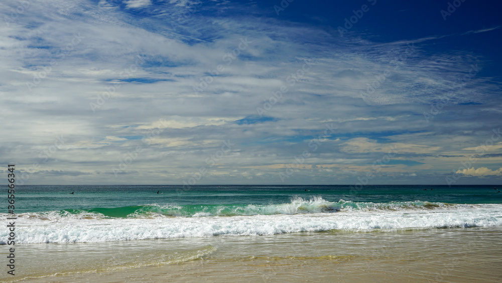 Expansive view from sandy beach across breaking waves to the horizon, under a beautiful blue cloudy sky.  Currumbin Beach, Gold Coast, Queensland, Australia.