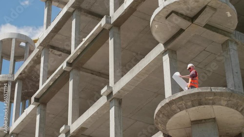 An architect in a protective suit at a height compares the plan of completed works with the drawing in his hands