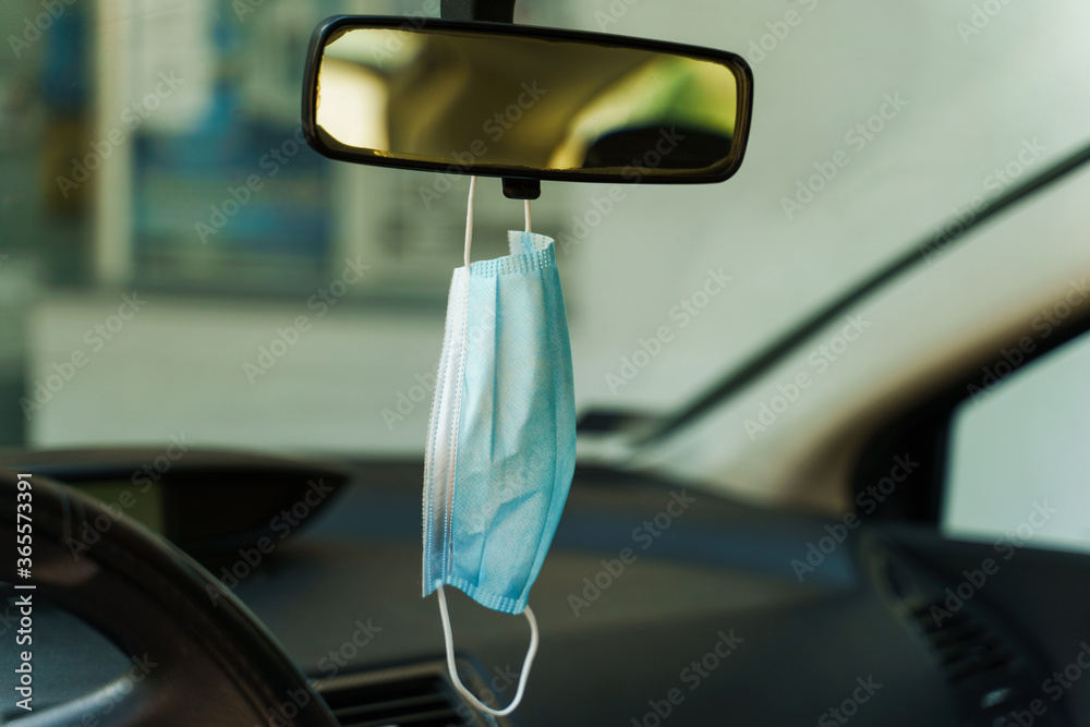 Medical protective face mask in car on the rearview mirror in day - Covid-19 pandemic protection on rear view in the vehicle - coronavirus epidemic new normal prevention concept Medical protective face mask in car on the rearview mirror in day - Covid-19 pandemic protection on rear view in the vehicle - coronavirus epidemic new normal prevention concept