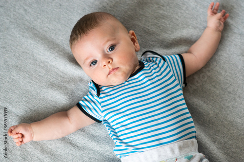 Obraz na płótnie Cute caucasian, blue eyed baby boy lying down on gray blanket with his arms spread open. Baby in striped outfit. w salonie