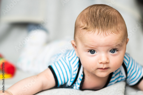 Obraz na płótnie Caucasian baby boy with blue eyes and brown hair playing on blanket while his tummy time, looking towards the camera. w salonie