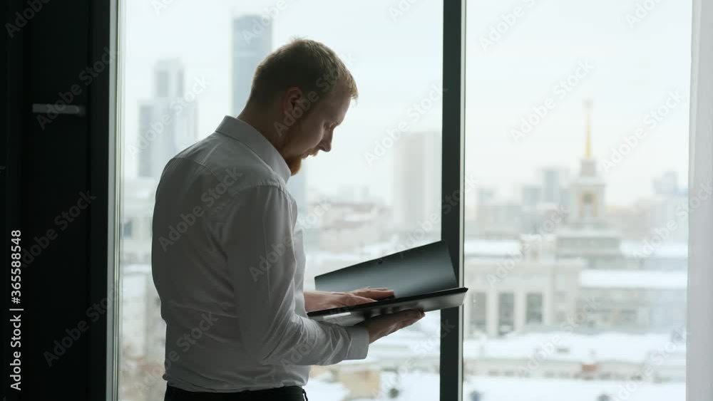 businessman holding a folder with documents while standing by a large window businessman holding a folder with documents while standing by a large window