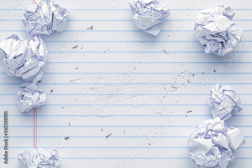 School supplies of blank lined notebook paper with eraser marks and erased pencil writing, surrounded by more trashed balled up paper. Studying or writing mistakes concept. photo