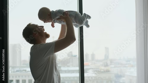 happy man picks up his child son while standing by the window