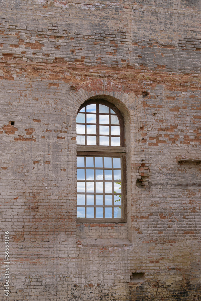 Vintage window overlooking the clouds. Wooden frame with small cells. Old red brick wall. Weathering, cracks. Concept of a medieval castle, antiquity.