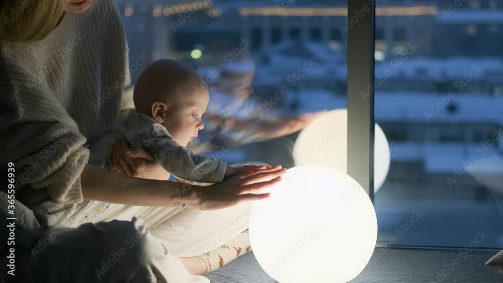 mom and baby touching the lamp balloon sitting by the window at night