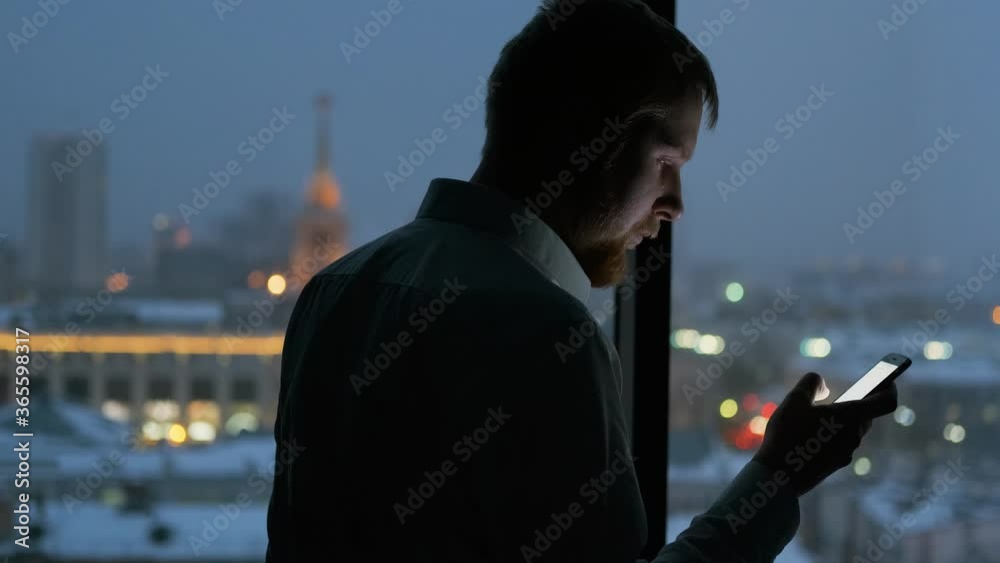 a man uses the phone by the window overlooking the city at night a man uses the phone by the window overlooking the city at night