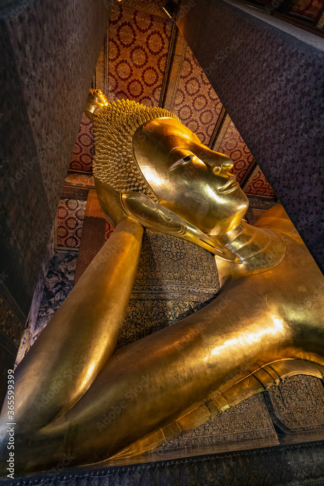 BANGKOK, THAILAND - JULY 28 2019: golden lying buddha sculpture, Phra Vihara of the Reclining Buddha within the monastic area of Wat Pho, Bangkok, Thailand.