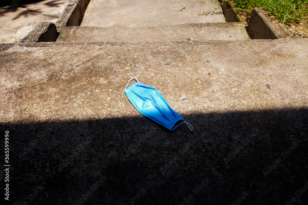 Blue face mask is left on the stairs, cement floor.