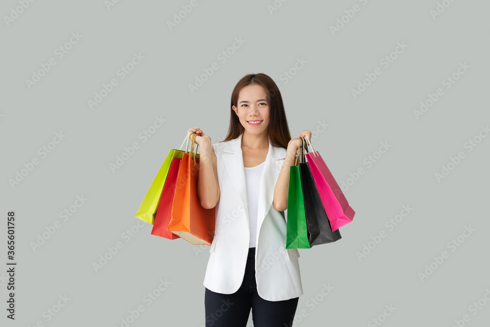 Portrait of smiling beautiful Asian woman holding shopping bags isolated over grey color background Portrait of smiling beautiful Asian woman holding shopping bags isolated over grey color background