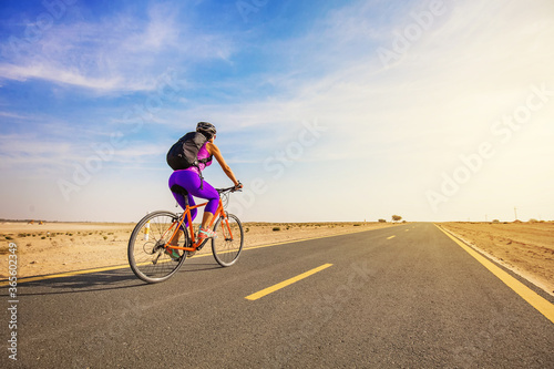 Young woman riding a bicycle in a desert in Dubai, full length shot