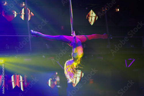 Flexible sexy athletic woman, aerial acrobatic hoop performance, women upside down on aerial hoop with high heels backlit in yellow light, air circus show. Perfect split upside down on aerial hoop
