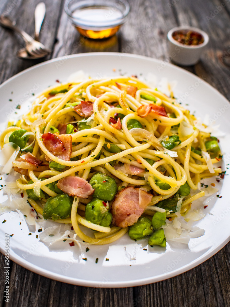 Spaghetti with broad bean, bacon and parmesan on wooden table
