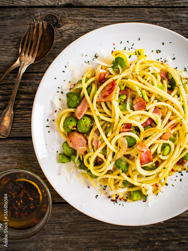 Spaghetti with broad bean, bacon and parmesan on wooden table
