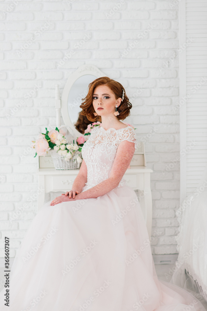 Portrait of red haired girl wearing wedding dress against a white studio background.