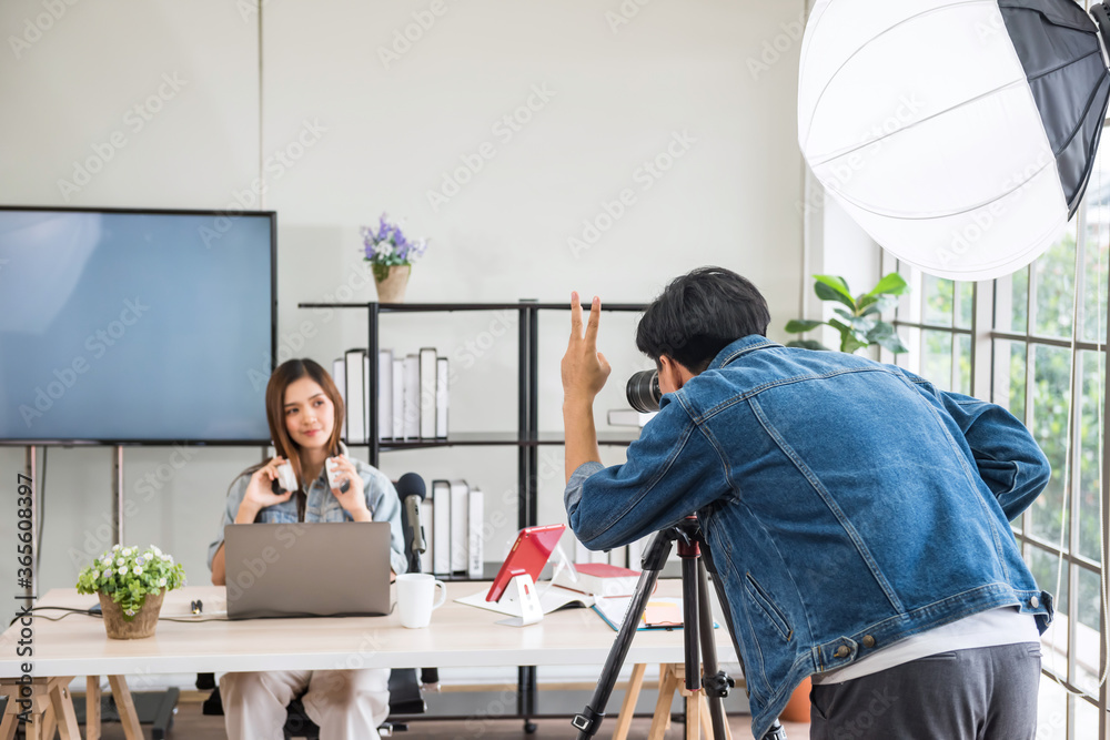 Fototapeta premium Video or professional digital camera man shoot or record live streaming of beautiful attractive Asian woman blogger podcaster with studio lighting. broadcasting for online journal or website content.