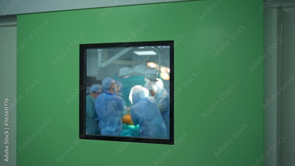 Surgery in the operating room. Teamwork of doctors in blue uniform doing an operation. View through the window from the corridor. Surgery in the operating room. Teamwork of doctors in blue uniform doing an operation. View through the window from the corridor.