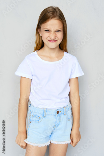 Young angry girl in white t-shirt and jeans shorts posing in studio