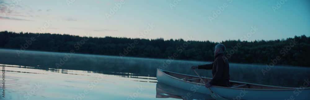 Man canoeing in a traditional wooden boat on a large lake at dawn, fog over water. Shot on RED cinema camera with 2x anamorphic lens Man canoeing in a traditional wooden boat on a large lake at dawn, fog over water. Shot on RED cinema camera with 2x anamorphic lens