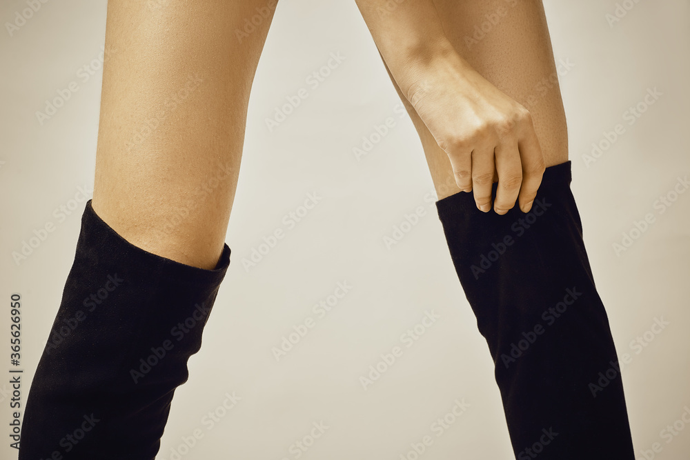 Beautiful female legs in black suede boots on a gray background.