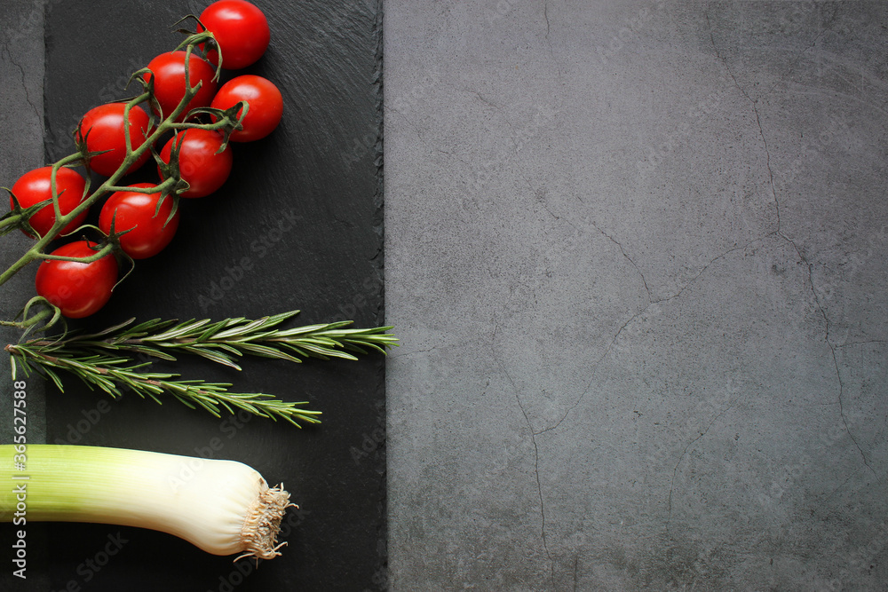 Bunch of cherry tomatoes, root of leek and rosemary on a black background. Menu concept. Top view. Copy space.