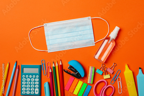 School supplies with medical mask and sanitizer on orange background