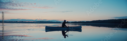 Photography Man canoeing in a traditional wooden boat on a large lake at dawn