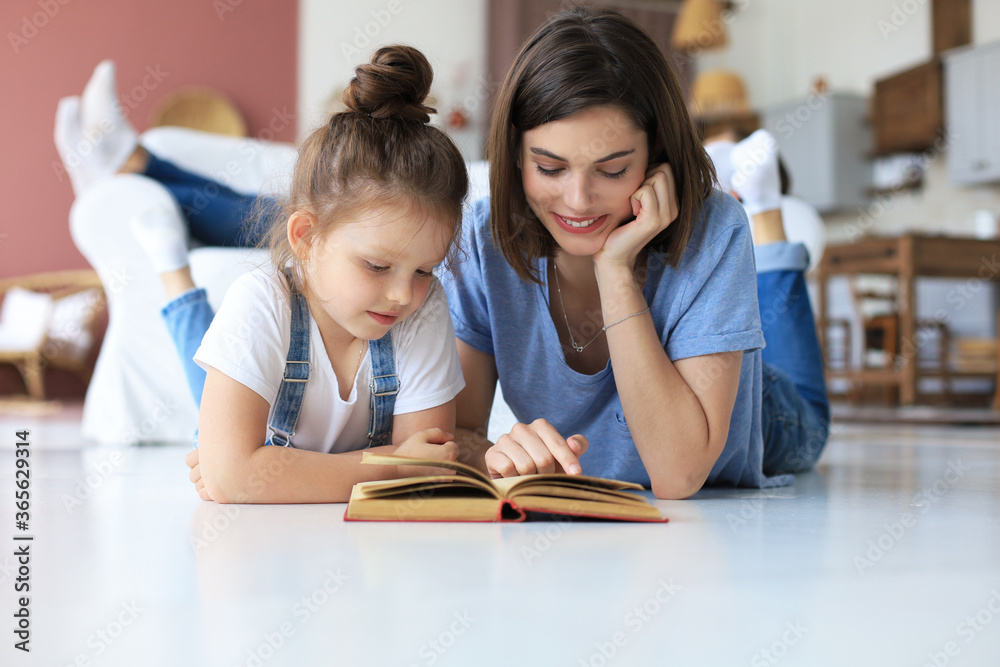 Mother and little daughter read a book together, lying on the floor in the living room. Mother and little daughter read a book together, lying on the floor in the living room.