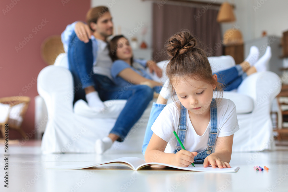 Smiling happy family sit relax on couch in living room watch little daughter drawing in album with colorful pencils. Happy weekends at home. Smiling happy family sit relax on couch in living room watch little daughter drawing in album with colorful pencils. Happy weekends at home.