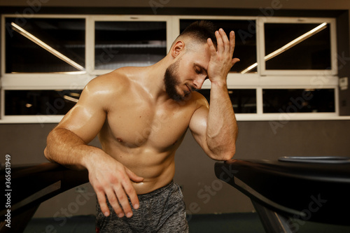 Young strong sporty man sitting on gym bench suffering and serious in a gym
