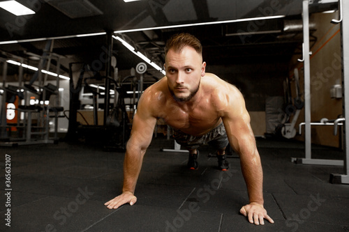 Sport motivation for people. Front view of young handsome man in sportswear doing push-up at gym
