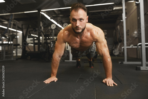 Sport motivation for people. Front view of young handsome man in sportswear doing push-up at gym. BE STRONG!