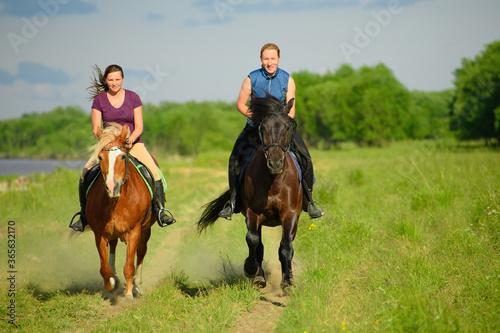 Two Caucasian horsewomen are riding along the rural road. The horses hooves are throwing up the dust-clouds. © Ирина Орлова