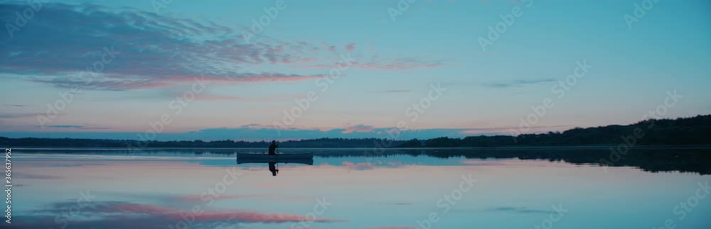 WIDE Man canoeing in a traditional wooden boat on a large lake at dawn. Shot on RED cinema camera with 2x anamorphic lens WIDE Man canoeing in a traditional wooden boat on a large lake at dawn. Shot on RED cinema camera with 2x anamorphic lens