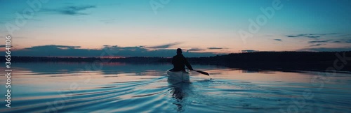 WIDE Man canoeing in a traditional wooden boat on a large lake at dawn. Shot on RED cinema camera with 2x anamorphic lens