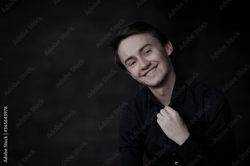 Happy young man. Close-up Portrait of handsome young smiling man in casual black shirt touching his collar and smiling while standing against black background. Lauphing handsome boy.