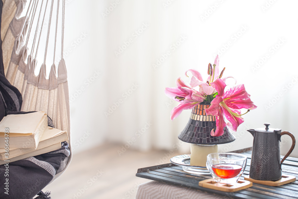 A boho-style hammock chair with a stack of books. Wooden tray with teapot and Cup of tea and beautiful Lily flowers. Cozy interior. The concept of rest and home comfort. A boho-style hammock chair with a stack of books. Wooden tray with teapot and Cup of tea and beautiful Lily flowers. Cozy interior. The concept of rest and home comfort.