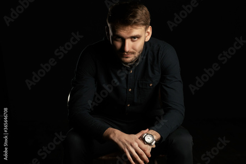 BE SUCCESSFUL. Handsome bearded charismatic man in black suit sitting on the chair and leaning his hands on legs against black background. Advertisment photo and banner with copy space. Studio shot © anessir