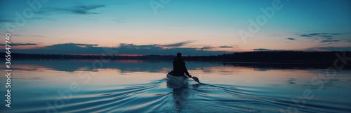 WIDE Man canoeing in a traditional wooden boat on a large lake at dawn. Shot on RED cinema camera with 2x anamorphic lens