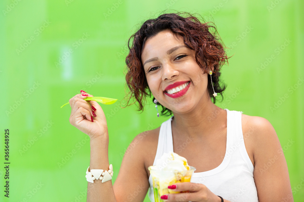 Close-up of smiling latin woman holding an ice cream on a green background. Space for text. Selective focus. Summer and lifestyle concept.