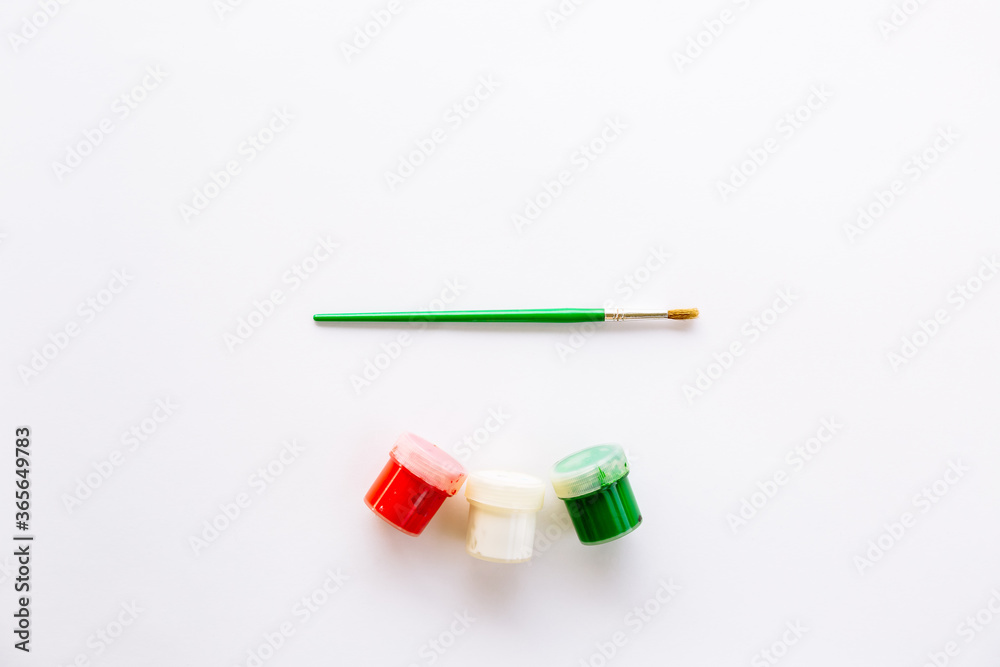 Three different colors white, red, green and brush for painting. Tools for painting or decorating in the New Year's palette. Jars with acrylic or gouache. Three different colors white, red, green and brush for painting. Tools for painting or decorating in the New Year's palette. Jars with acrylic or gouache.