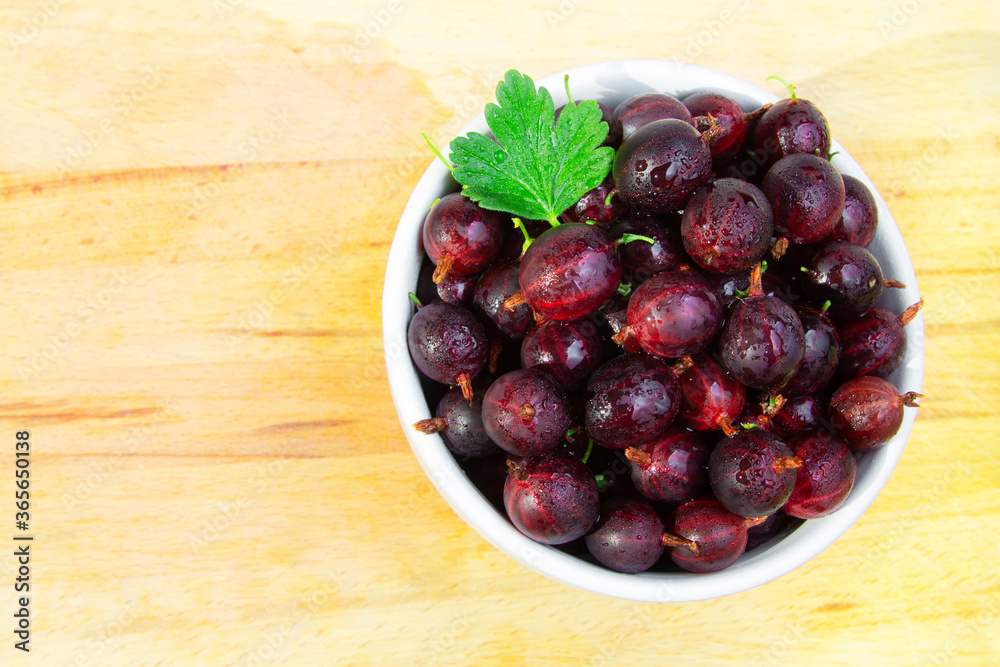 Fresh red gooseberries in a cup on a wooden background Fresh red gooseberries in a cup on a wooden background
