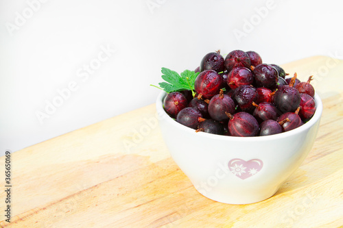 Fresh red gooseberries  in a cup on wooden background