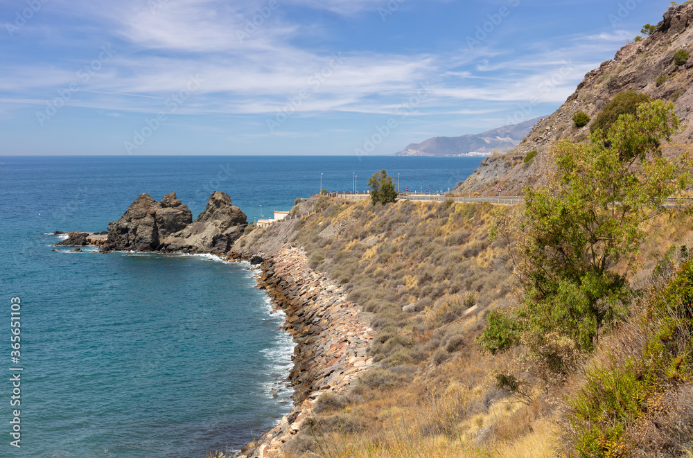 The beautiful and rocky coast in southern Spain in Andalusia. The water and the sky are blue when the sun shines. In the distance you can see the city of Motril. The beautiful and rocky coast in southern Spain in Andalusia. The water and the sky are blue when the sun shines. In the distance you can see the city of Motril.