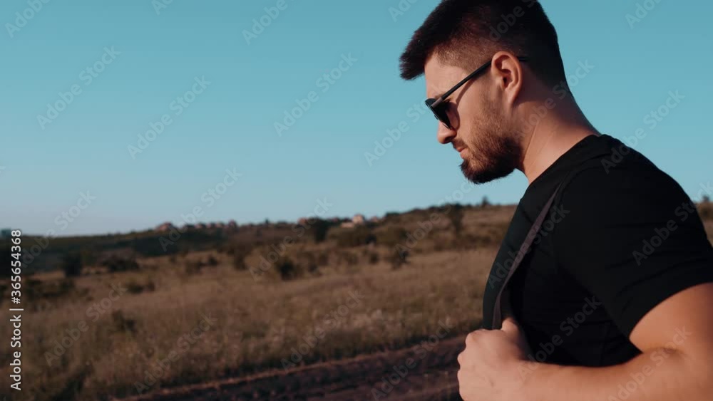 A portrait of a young man walking through the middle of a field. Active male tourist with backpack walking in the natural field. A portrait of a young man walking through the middle of a field. Active male tourist with backpack walking in the natural field.