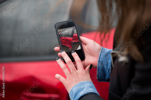 Woman using a smart phone to take a photo of the damage to her car caused by a car crash