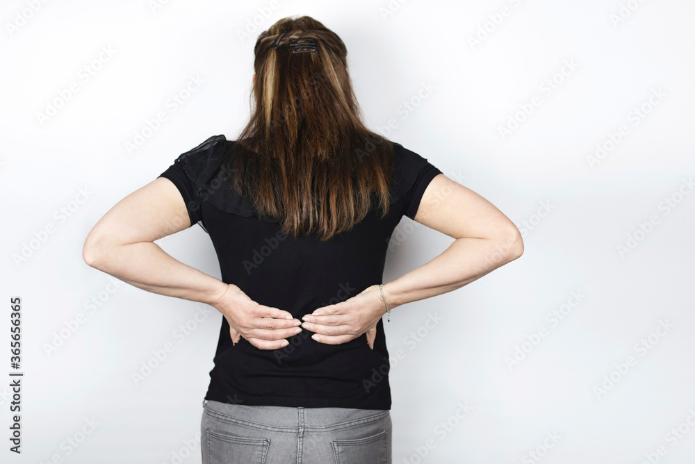 The woman is holding her back with both hands because she is experiencing severe sharp pain in her lower back. The woman sits all day at work and moves little. Rear view The woman is holding her back with both hands because she is experiencing severe sharp pain in her lower back. The woman sits all day at work and moves little. Rear view