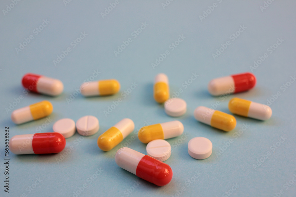 Multicolored pills and capsules on blue background with copy space. Top view, selective focus

